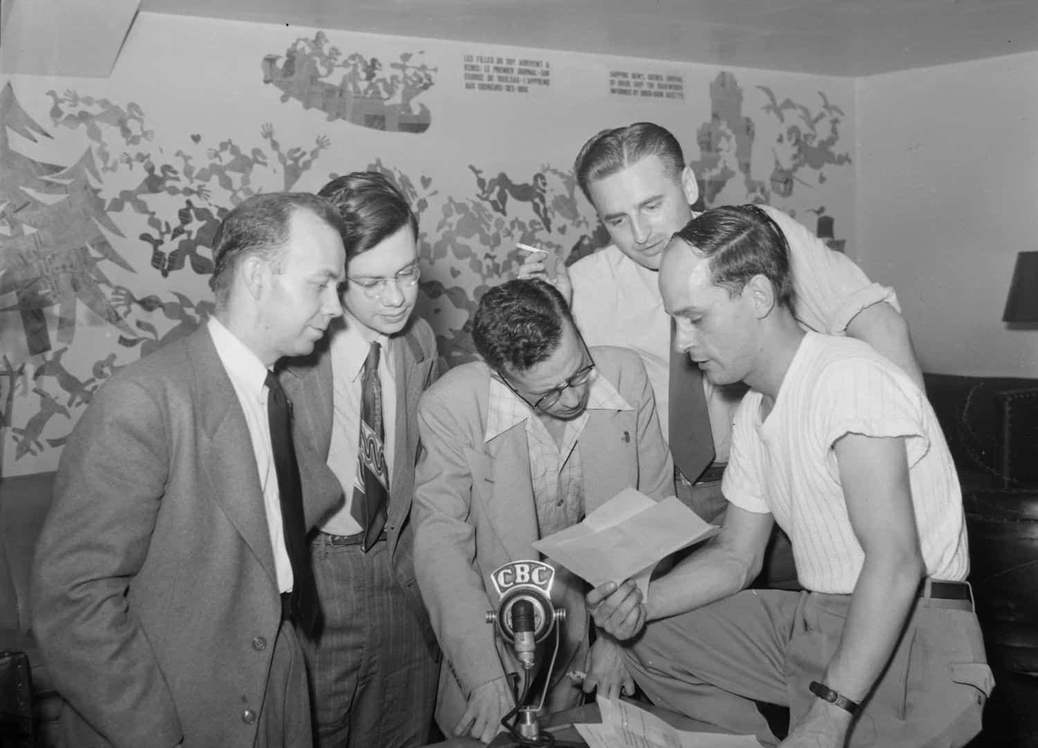 René Lévesque (à droite) montre un document à ses collègues du Cercle des journalistes de Montréal, réunis autour d’un micro de CBC, en juin 1949.