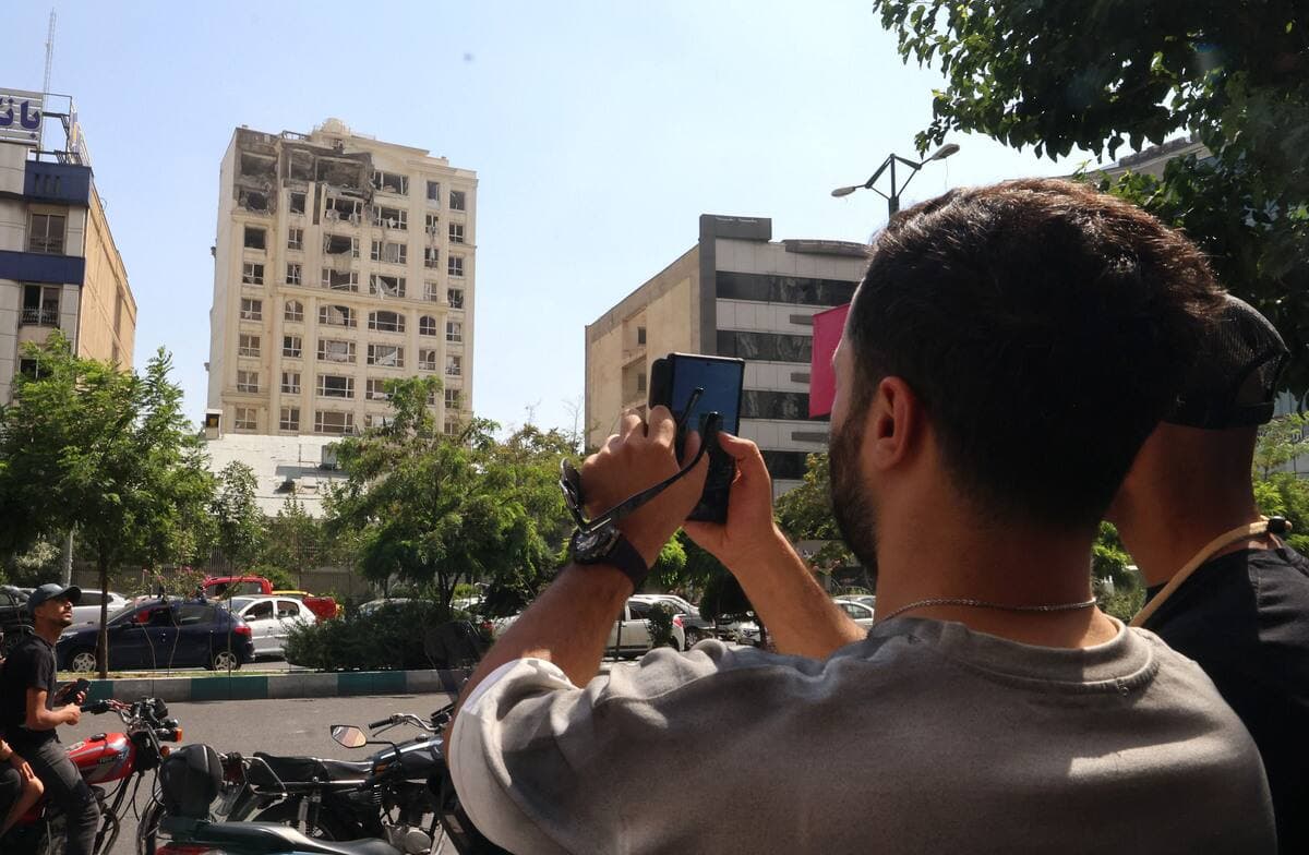 Un homme prend une photo d'un bâtiment endommagé lors d'une frappe israélienne sur Téhéran le 13 juin 2025. Israël a frappé environ 100 cibles en Iran le 13 juin, notamment des installations nucléaires et des centres de commandement militaire, tuant des personnalités de haut rang, dont le chef des forces armées et de hauts scientifiques nucléaires.