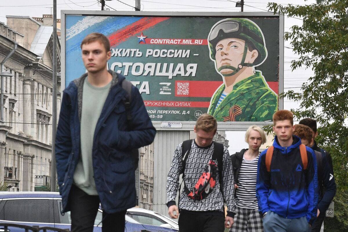 De jeunes Russes marchent devant un panneau publicitaire faisant la promotion du service militaire, à Saint-Pétersbourg. «Servir la Russie est un vrai job», dit la publicité.
