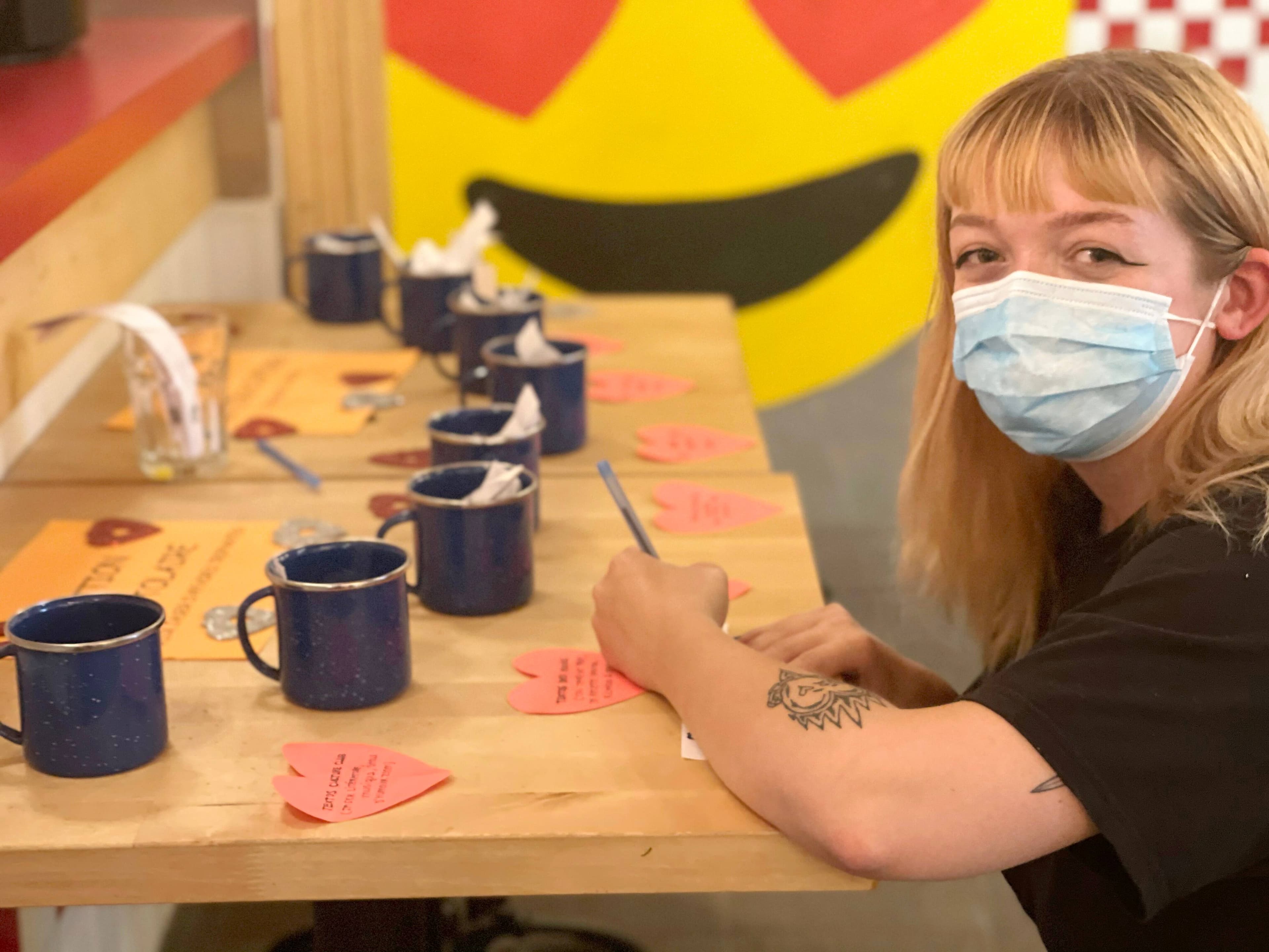Les participants du jeu de rencontre inscrivent leur nom et leurs coordonnées sur un petit papier qu’ils déposent dans l’une des tasses d’où quelqu’un finira par le tirer, comme le fait ici (pour la photo seulement) la barista de La graine brûlée, Justine Lepage-Roy.