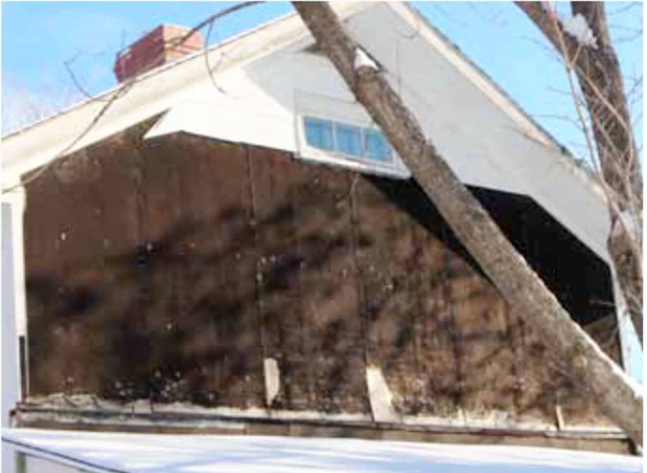 Une large section de tuiles est tombée, au-dessus de la véranda, exposant le papier noir du revêtement.