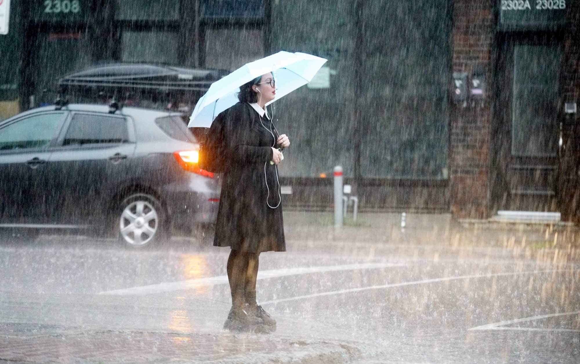 Une femme attend de pouvoir traverser dans le déluge montréalais jeudi.