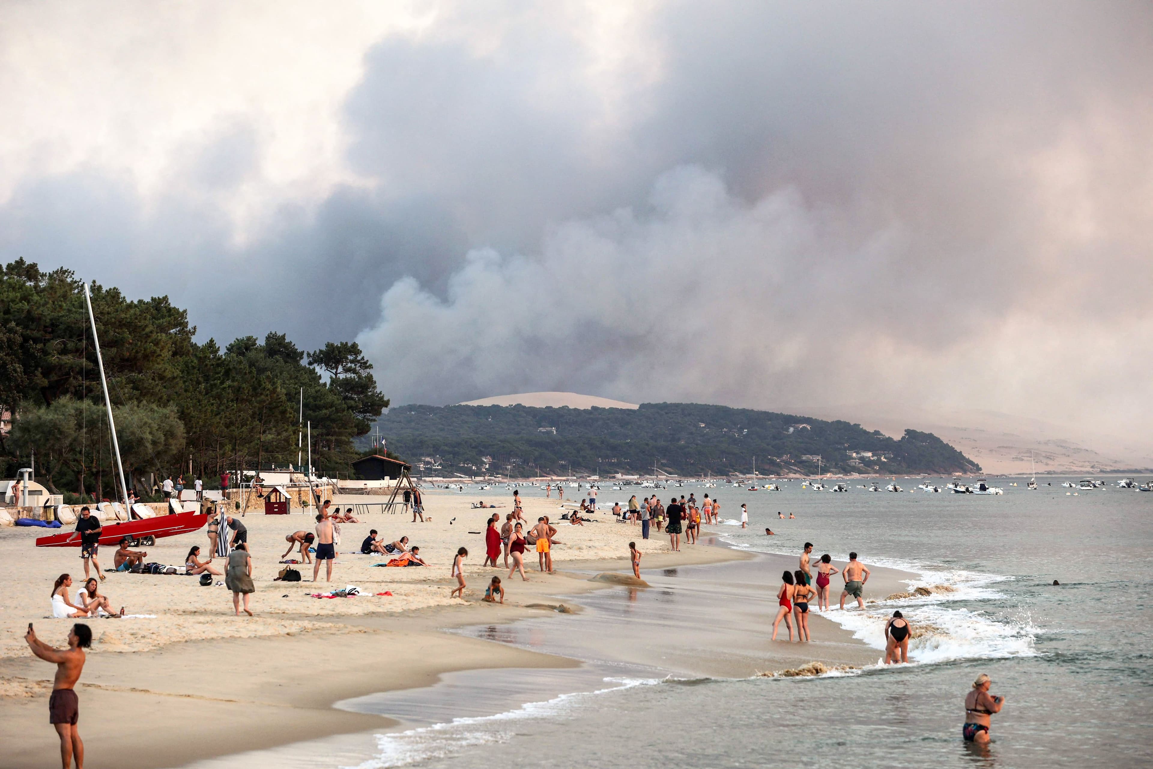 Des vacanciers se baignent sur la plage du Moulleau, dans le bassin d’Arcachon en France, en regardant l’épaisse fumée de l’incendie d’une forêt voisine.