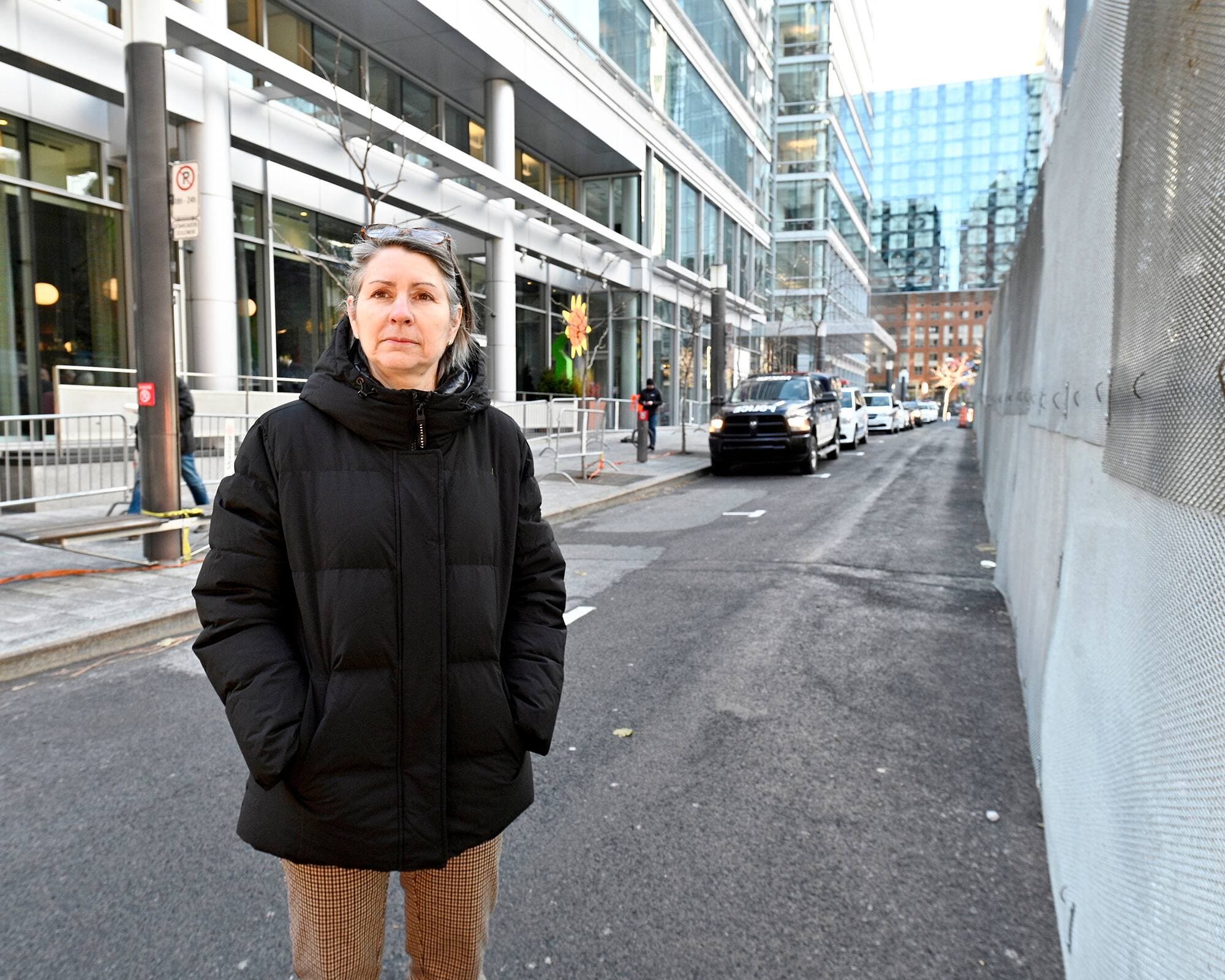 Christine Lamarche, copropriétaire du restaurant Toqué!, pose à côté d’une clôture installée devant le restaurant pour la sécurité, avec des policiers derrière elle.