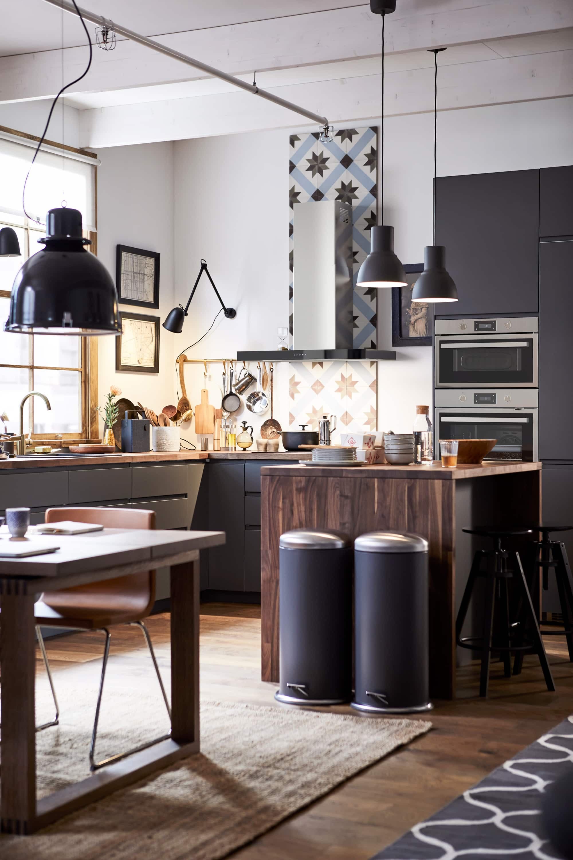 Une lampe articulée posée au mur apporte un accent industriel.
C’est tendance : les armoires noires au fini mat.
Une bande étroite de céramique à motifs crée un bel accent sous la hotte.
Une carpette circonscrit la zone salle à manger.