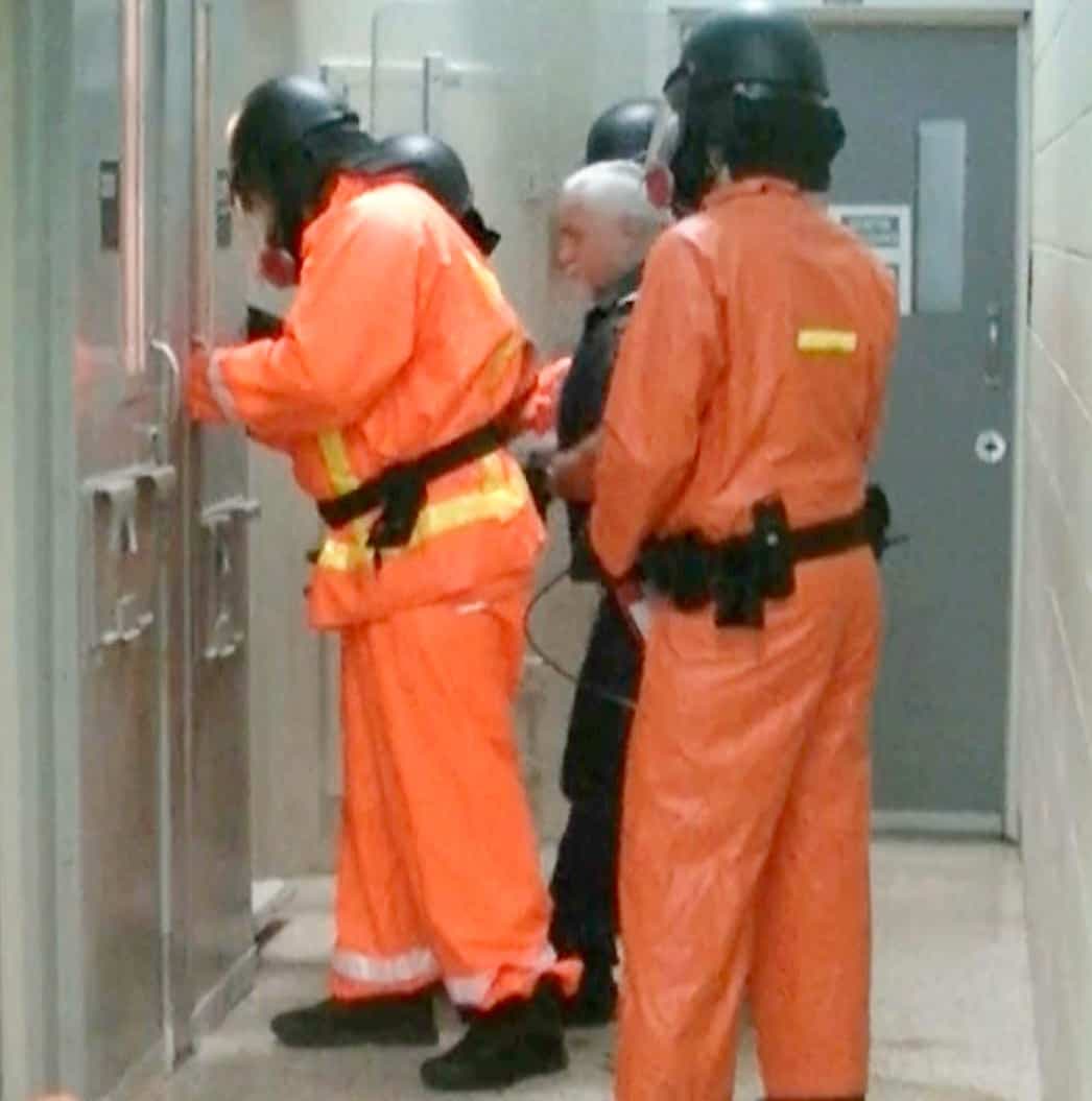 À l’été 2018, des agents correctionnels s’apprêtent à intervenir auprès du détenu et sont prêts à utiliser les gaz en cas de besoin. Ils portent masque et combinaisons protectrices.