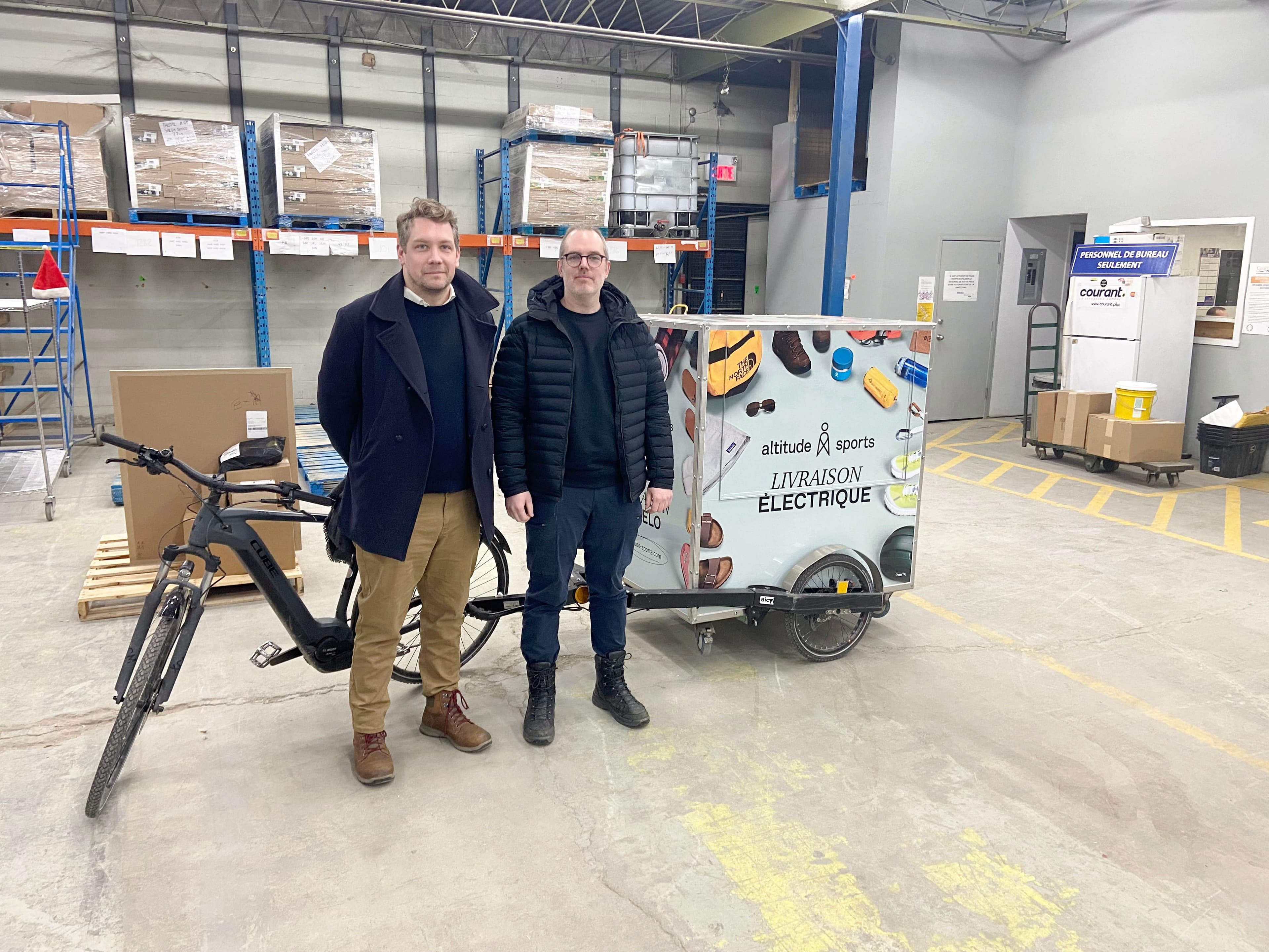 Edwin Richard, de Courant Plus, et Alexandre Guimond, d’Altitude Sports, posent devant l’un des vélos électriques que va utiliser le transporteur pour livrer les colis du détaillant en ligne.