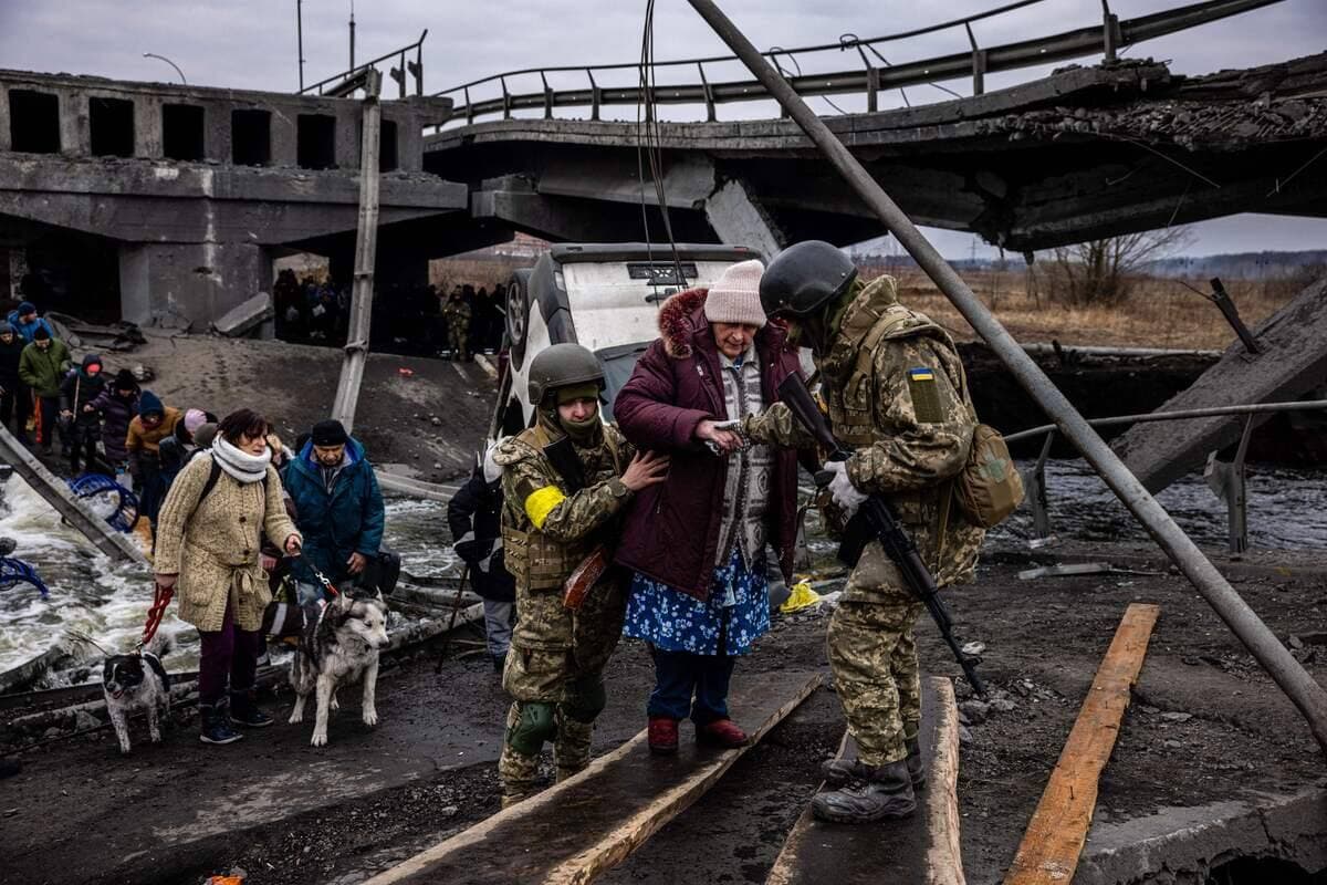 Des soldats ukrainiens aident une femme à traverser un pont détruit par des frappes russes alors qu'elle évacue de la ville de Irpin.