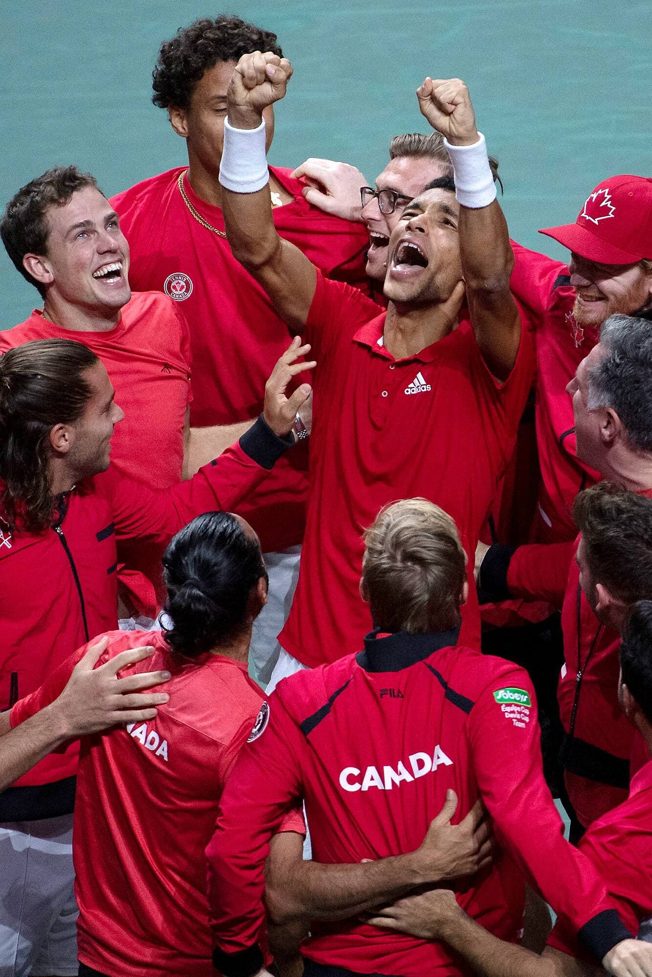 Entouré de ses coéquipiers, Félix Auger-Aliassime lève les bras vers le ciel, tandis qu’on voit Vasek Pospisil être ému à côté de lui.